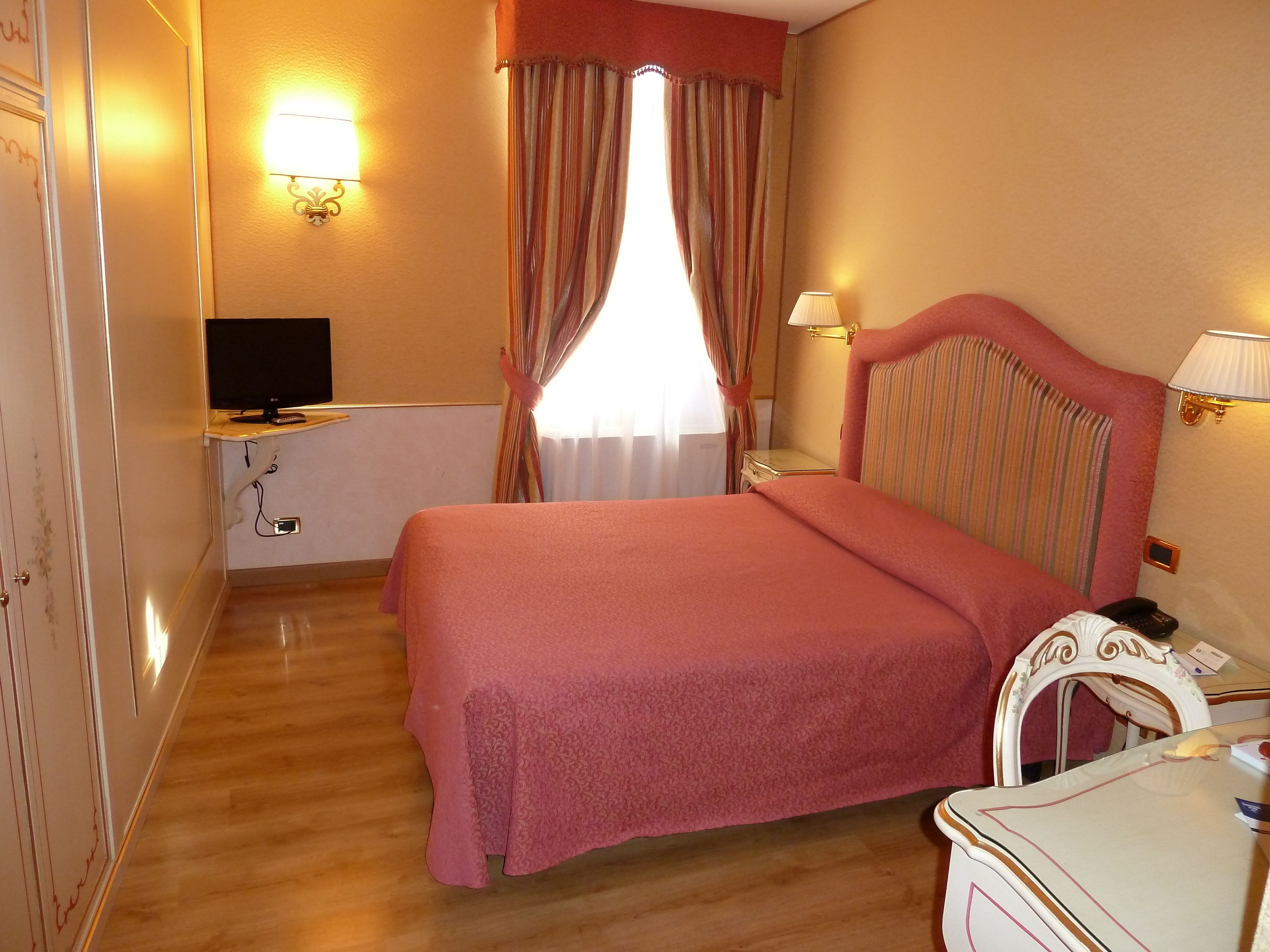 Ein Hotelzimmer mit einem Bett, einem Schreibtisch mit Computer, einem Telefon und einer Lampe.