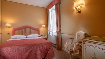 Una habitación de hotel con una cama grande, dos lámparas de noche, una silla y un aparador.