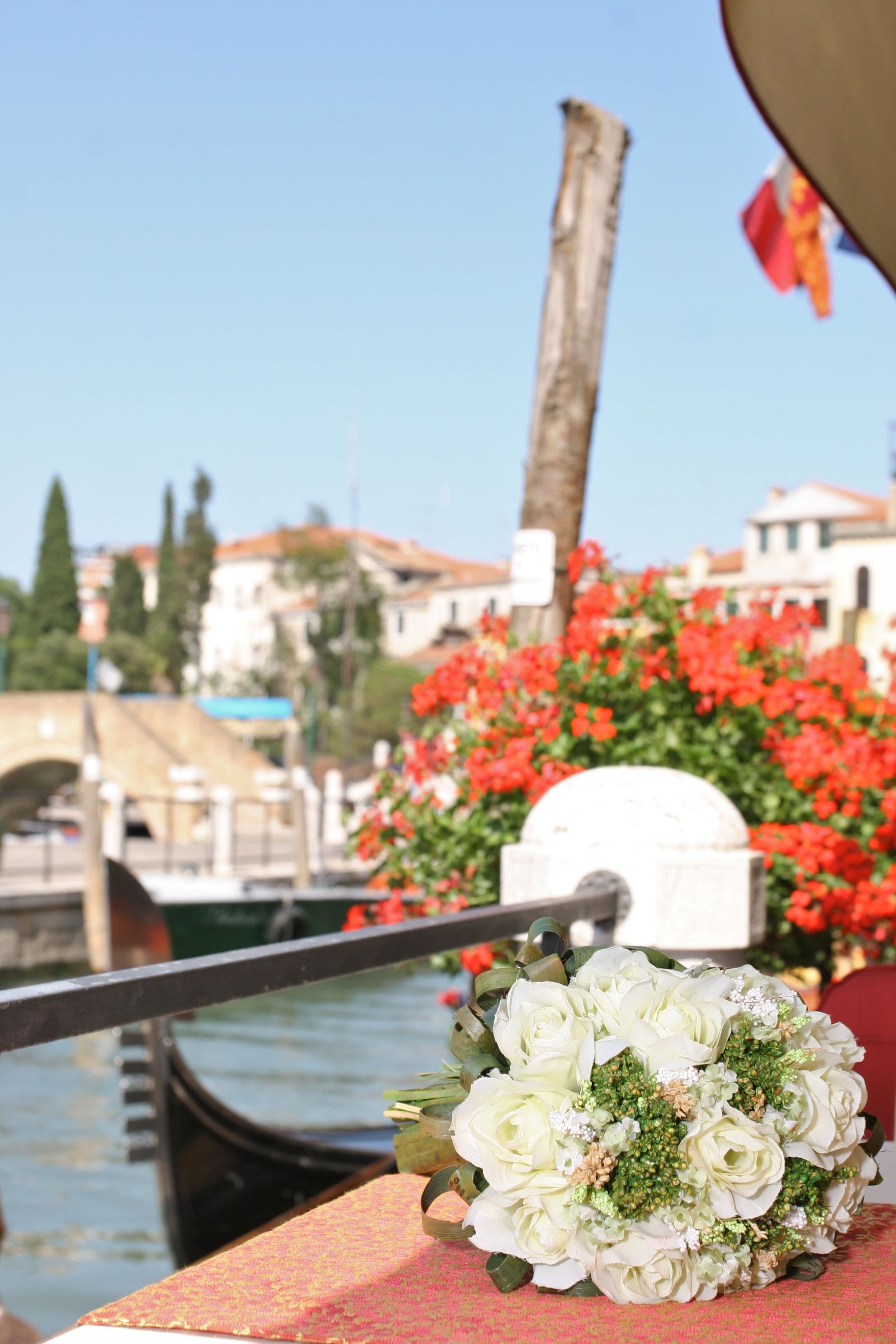 Une gondole sur un canal, avec un bouquet de fleurs posé sur la rambarde.