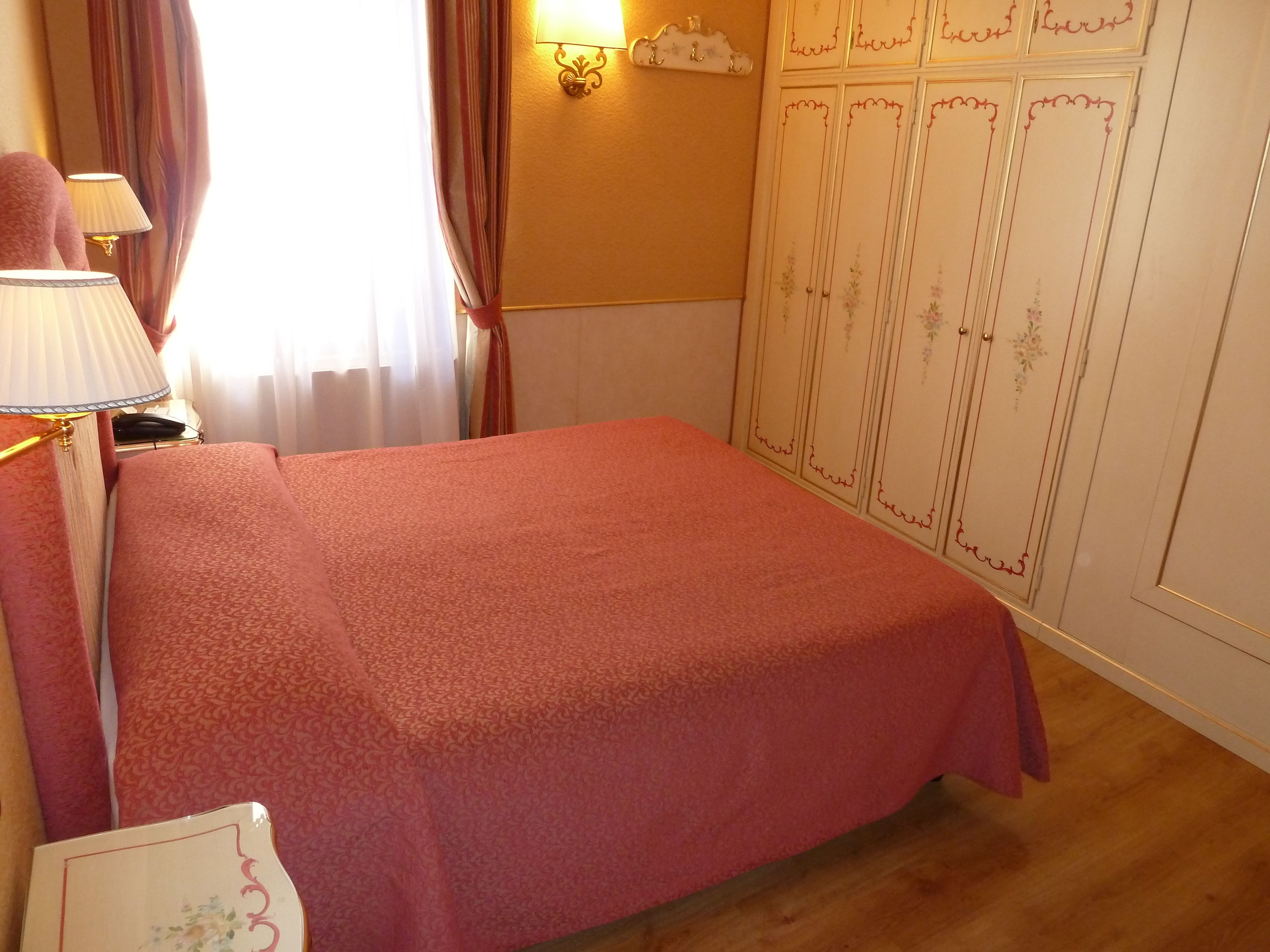 A bedroom with a bed, a nightstand, a lamp, a wardrobe, and curtains.