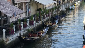 A canal with gondolas moored along the side, a hotel with a sign reading "Hotel", and a snack bar with outdoor seating. - Alloggi Olimpia (Venice)
