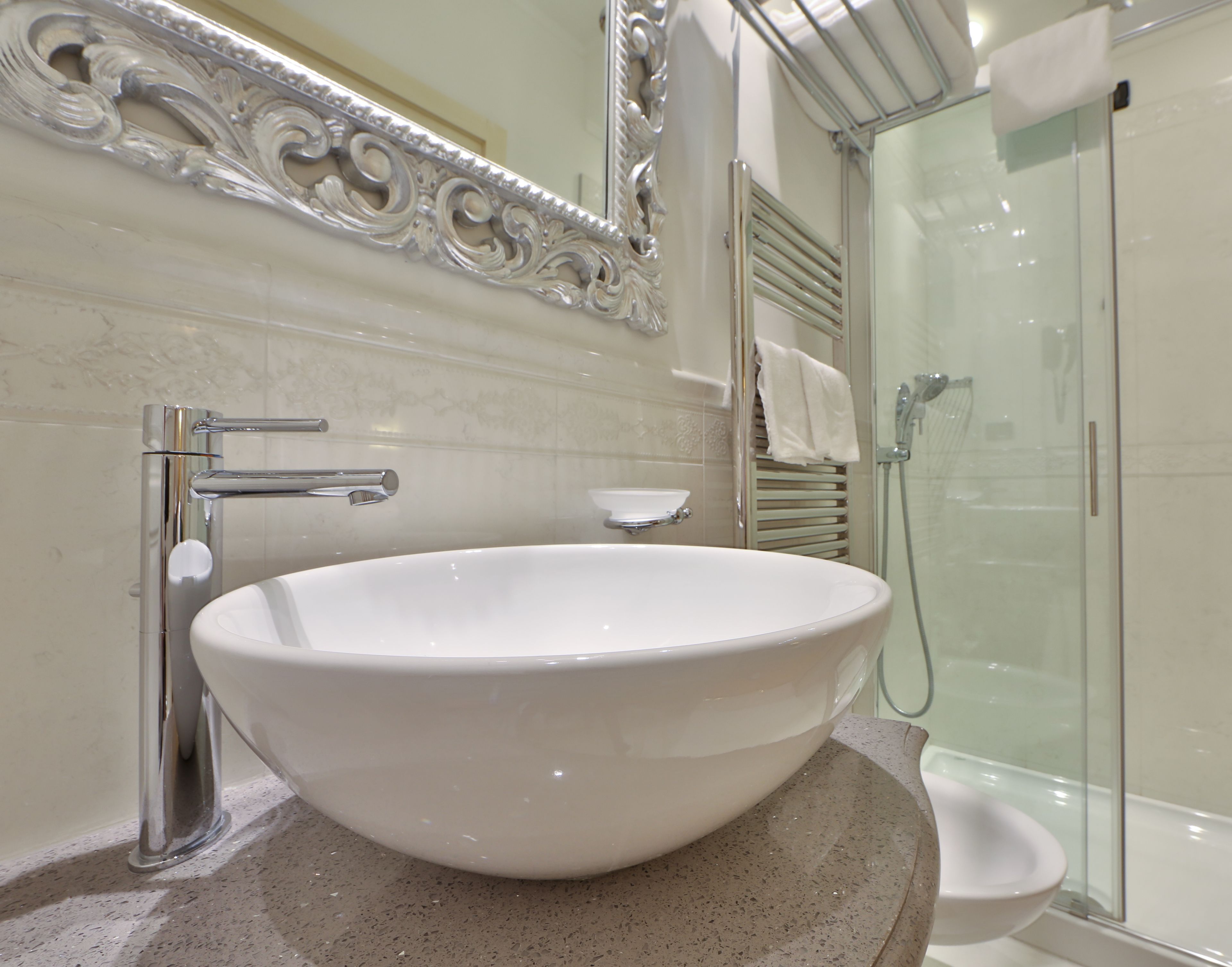 A bathroom with a large white sink, a mirror with ornate detailing, and a glass-enclosed shower.