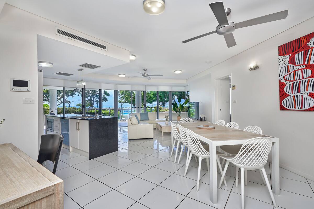A modern kitchen with a dining area, large windows, and a view of the ocean.