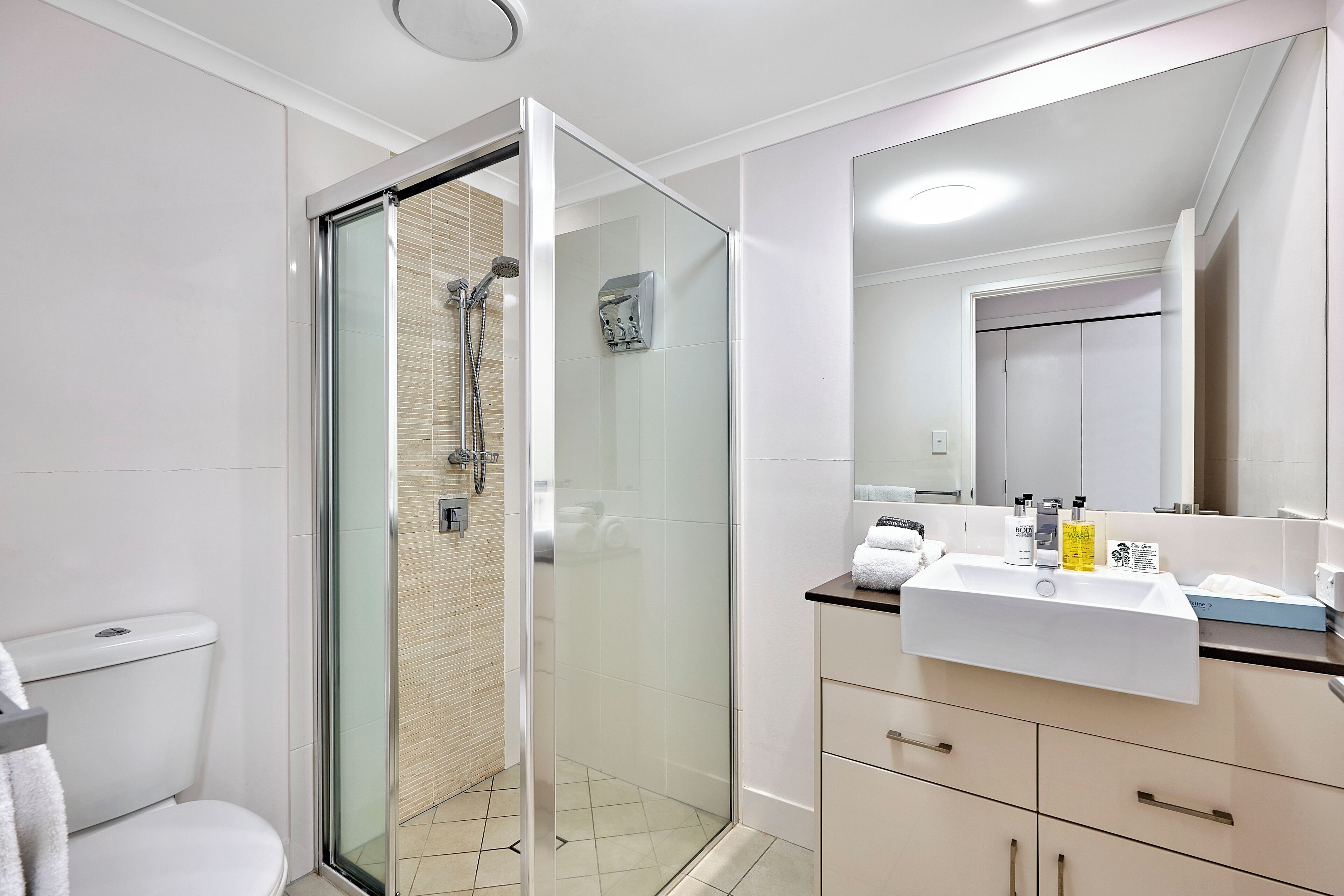 Un baño moderno con ducha de vidrio, lavabo blanco y un espejo grande.
