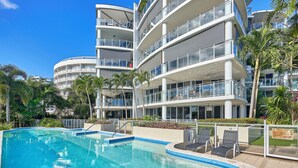 Un hotel moderno con piscina, numerosi balconi e palme.