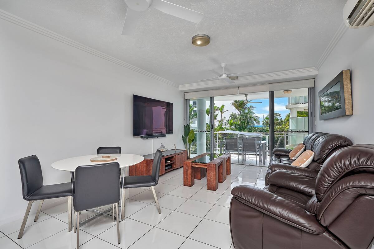A modern living room with a dining area, a sofa, and a TV mounted on the wall.