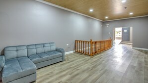 A spacious room with a wooden ceiling, a grey sofa, and a wooden railing.