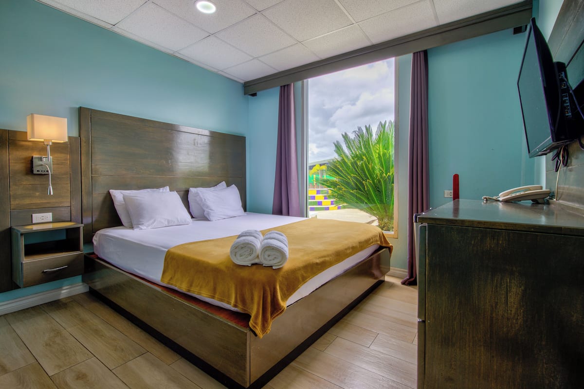 A hotel room with a bed, a nightstand, a desk, a television, and a window with curtains.