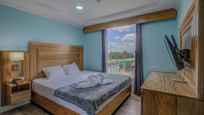 A hotel room with a wooden bed, a desk with a TV, and a window with a view of the outside.