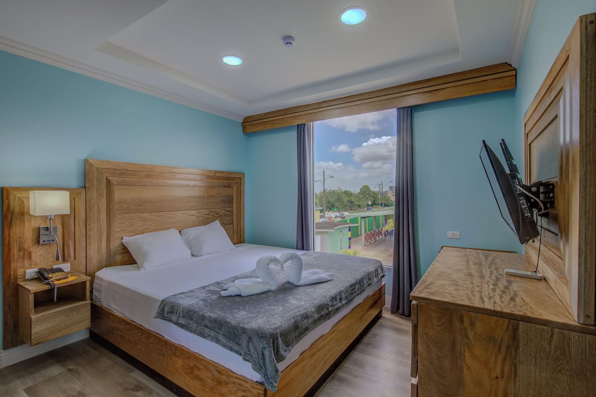A hotel room with a wooden bed, a desk with a TV, and a window with a view of the outside.