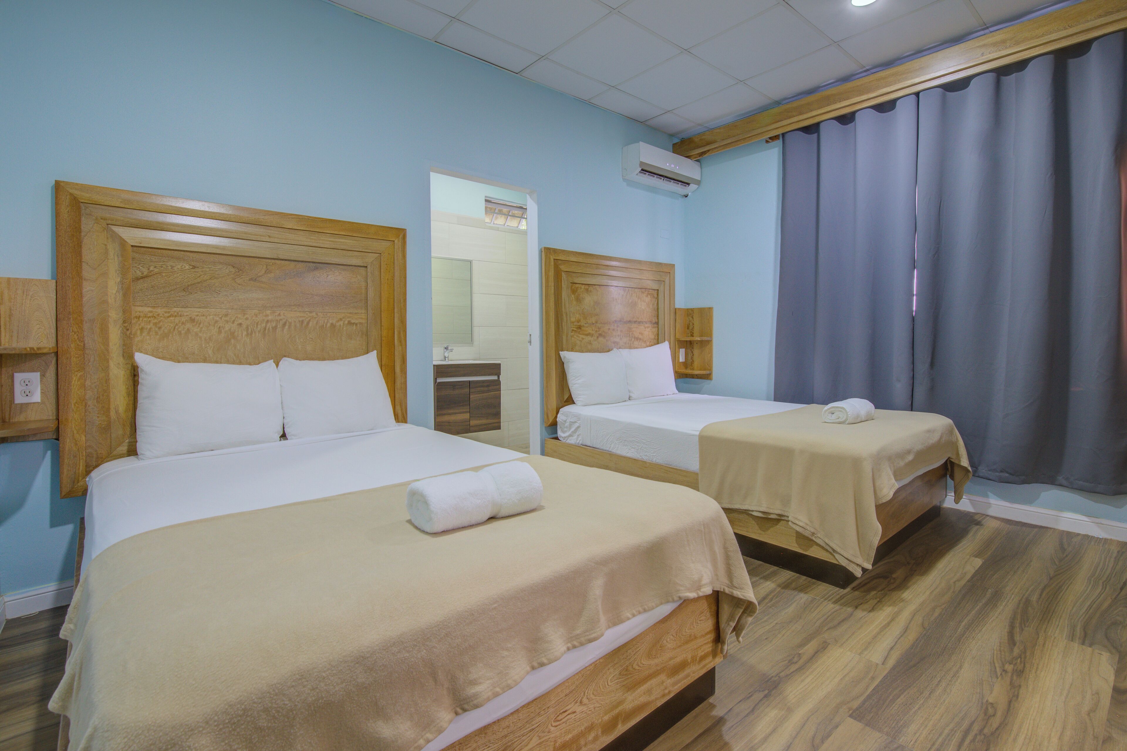 Une chambre d’hôtel avec deux lits, des têtes de lit en bois, un miroir et une fenêtre avec des rideaux.
