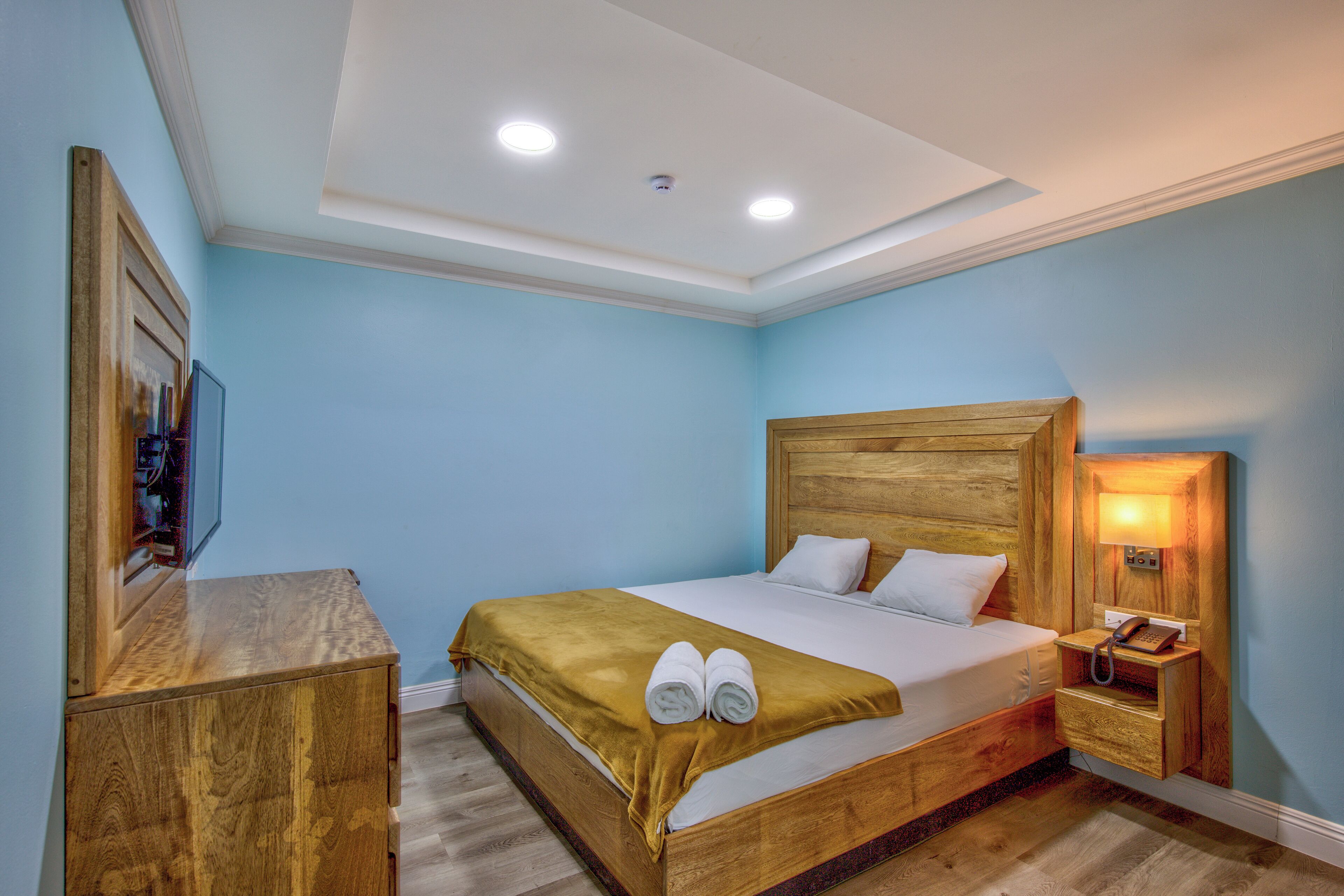 A neatly arranged bedroom with a wooden bed, a bedside table, a nightstand, and a wall-mounted lamp.