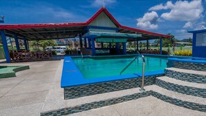 A swimming pool with a tiled deck and a covered area with a red roof.