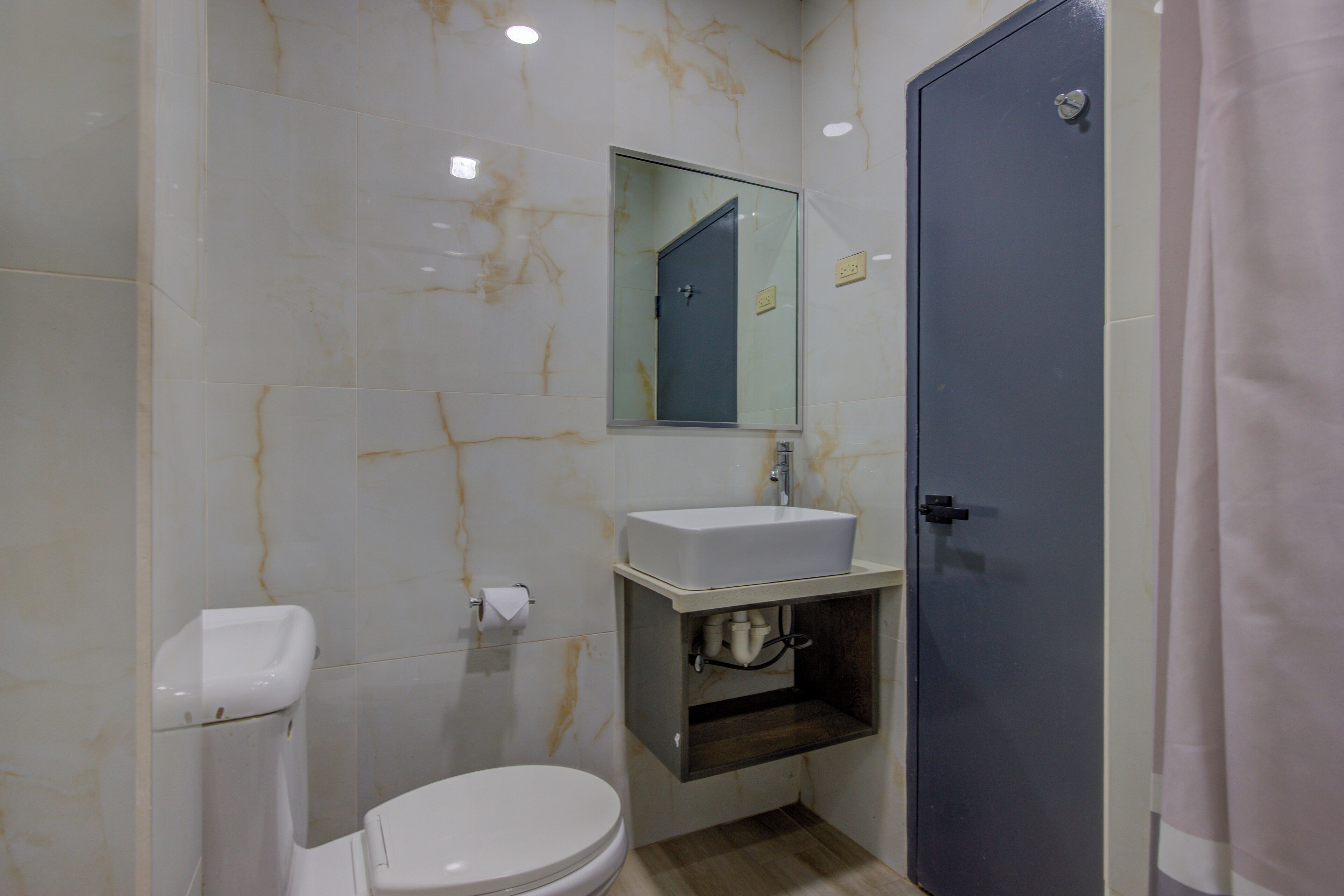A bathroom with a toilet, sink, mirror, and a door.