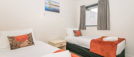 Habitación de hotel con dos camas, una mesita de noche pequeña, una ventana con cortinas y un cuadro en la pared.
