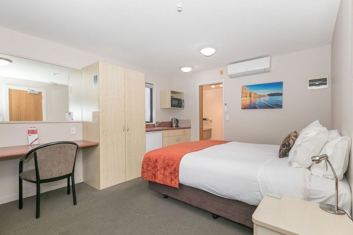 Hotelkamer met een bed, bureau, stoel, kitchenette en badkamer.