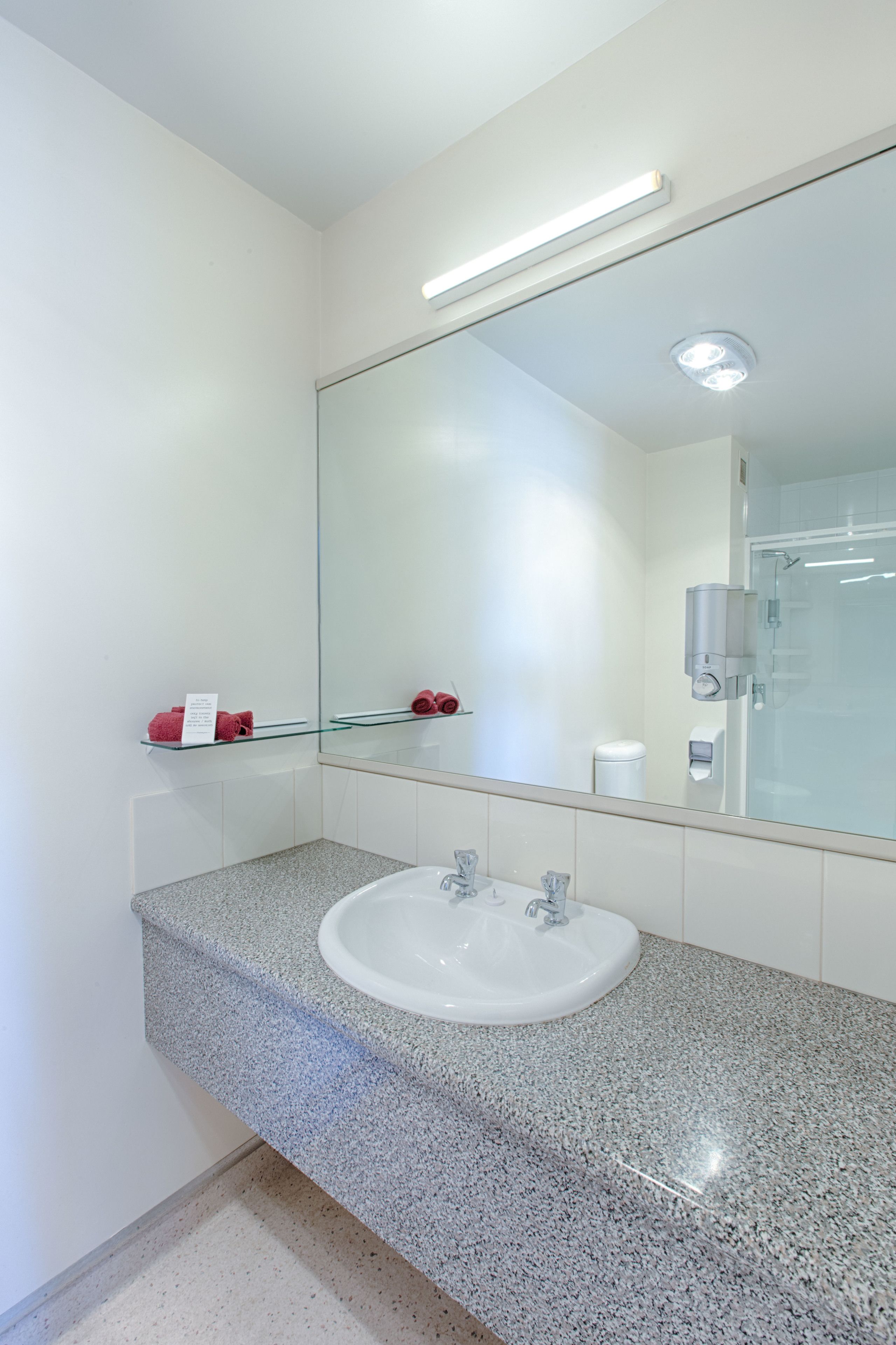 A modern bathroom with a granite countertop, white sink, and a large mirror.
