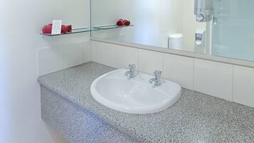 A modern bathroom with a granite countertop, white sink, and a large mirror.