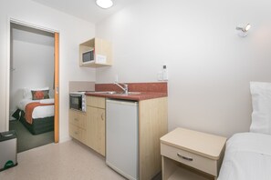 Una habitación de hotel compacta con kitchenette, una cama, una mesita de noche pequeña y un armario.
