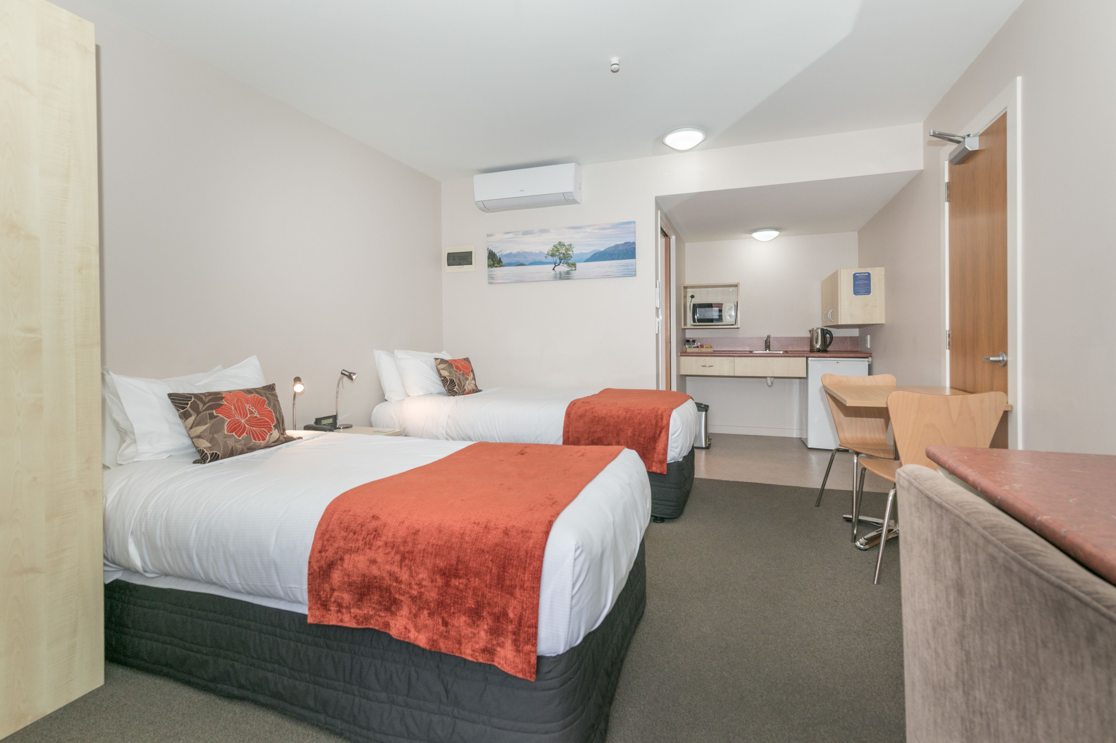 A hotel room with two beds, a desk, a chair, and a kitchenette.