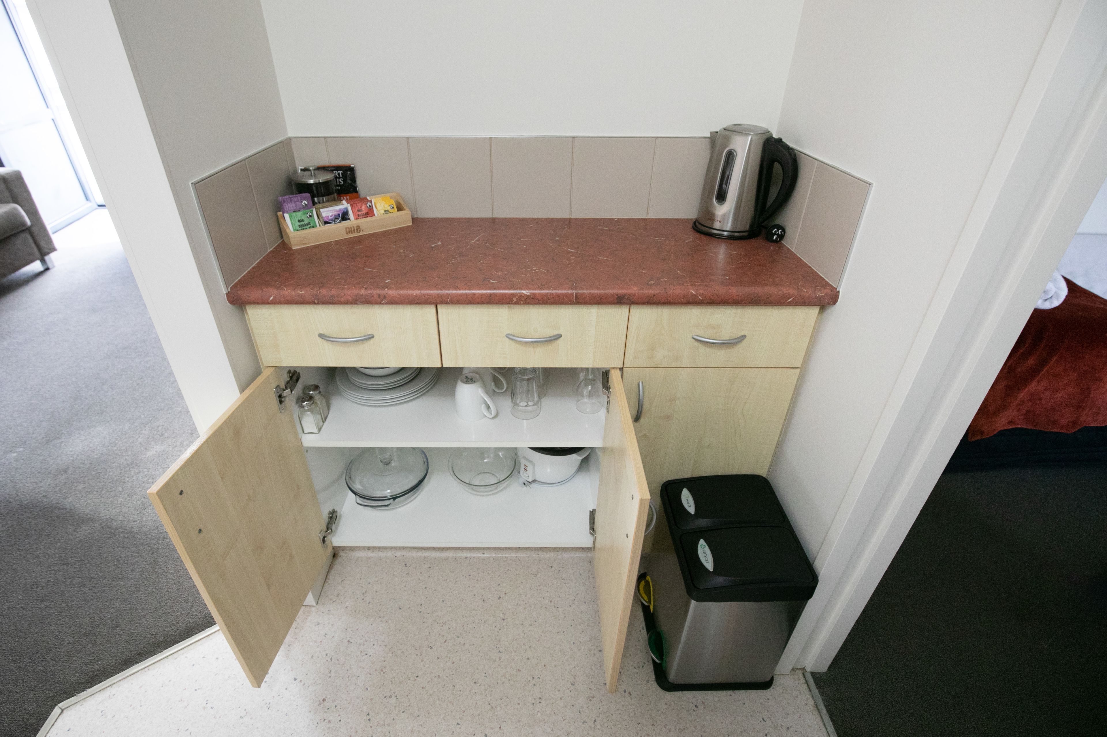 A compact kitchen with a wooden countertop, three drawers, and a trash bin.