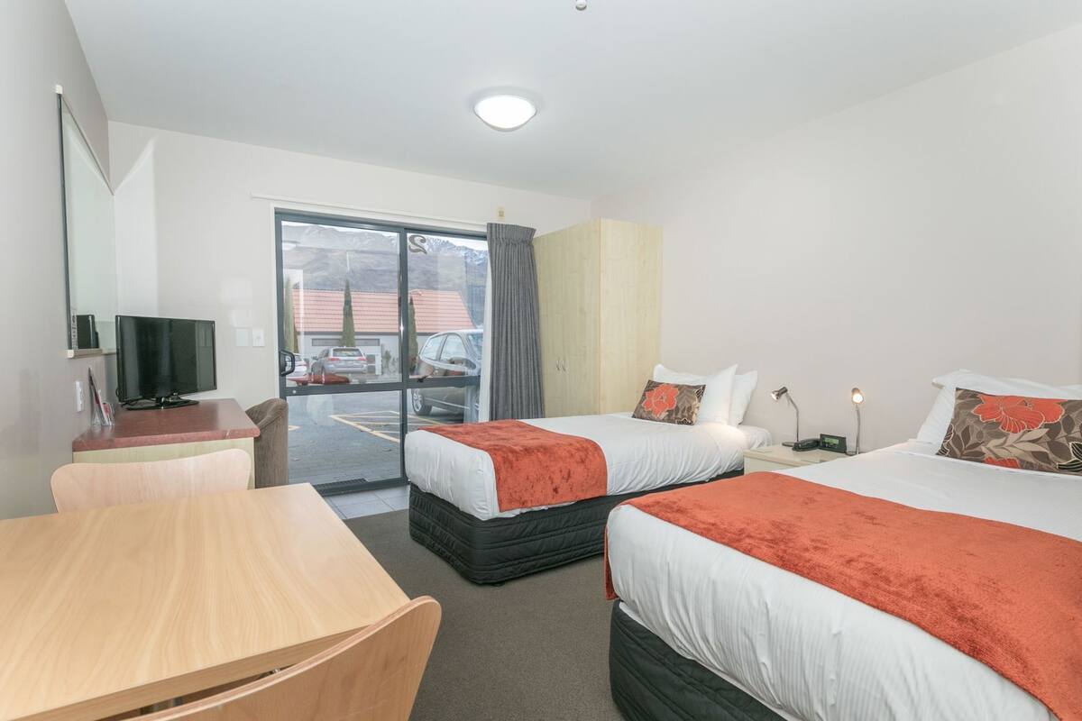Een hotelkamer met twee bedden, een bureau, een televisie en uitzicht op de parkeerplaats.