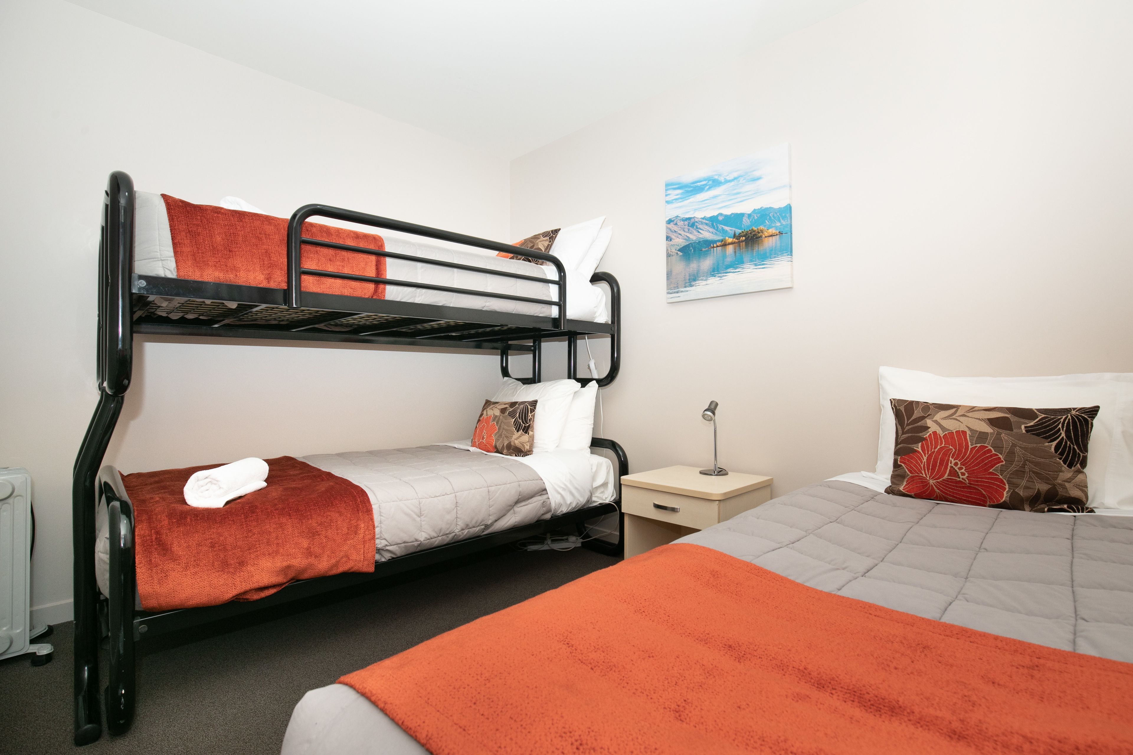 A bunk bed room with a nightstand, a lamp, and a painting on the wall.
