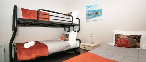 A bunk bed room with a nightstand, a lamp, and a painting on the wall.