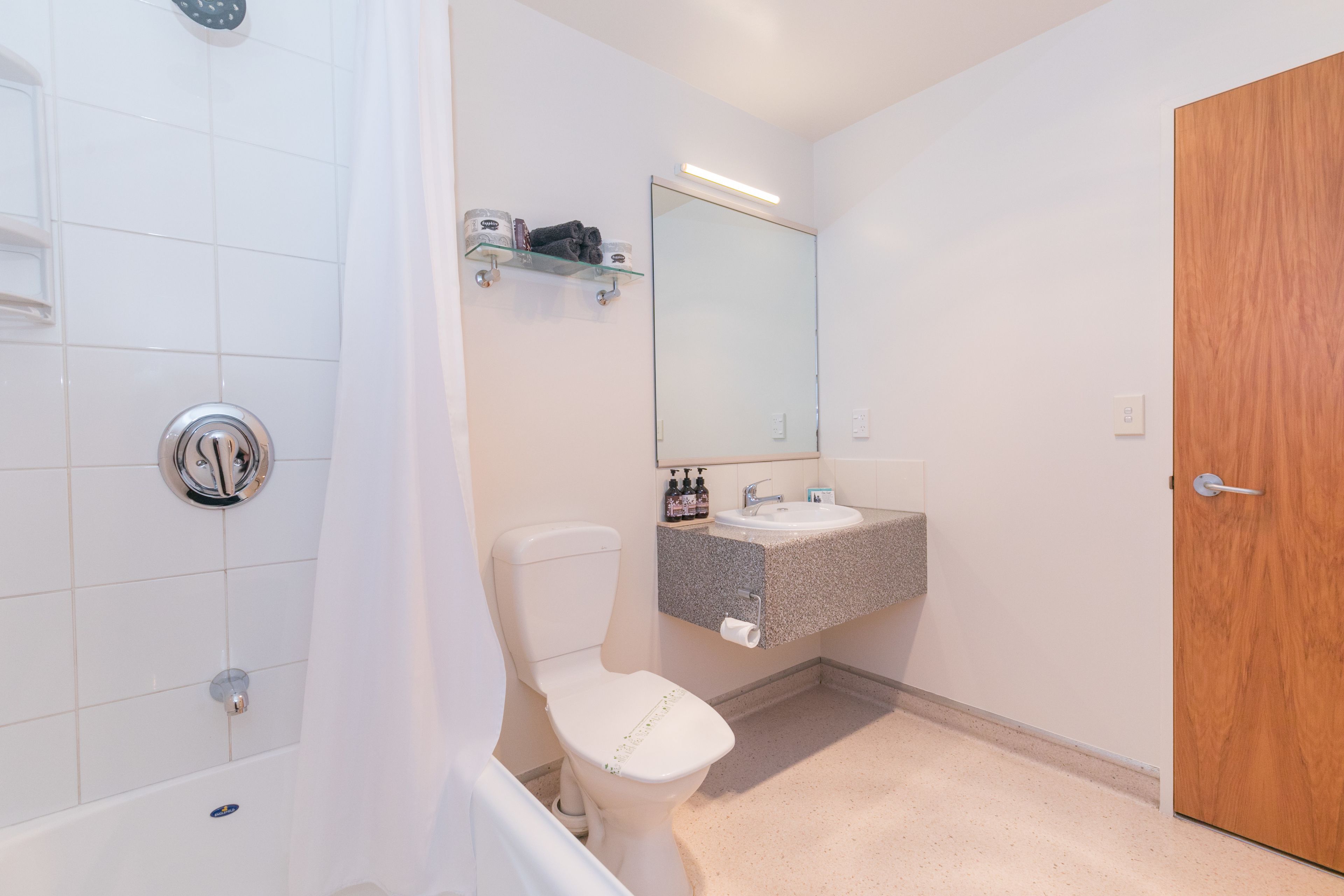 Een badkamer met douche, toilet, wastafel en een houten deur.