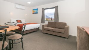 A hotel room with a bed, a sofa, a dining table with chairs, and a window with curtains. - Bella Vista Motel Wanaka (Wanaka)