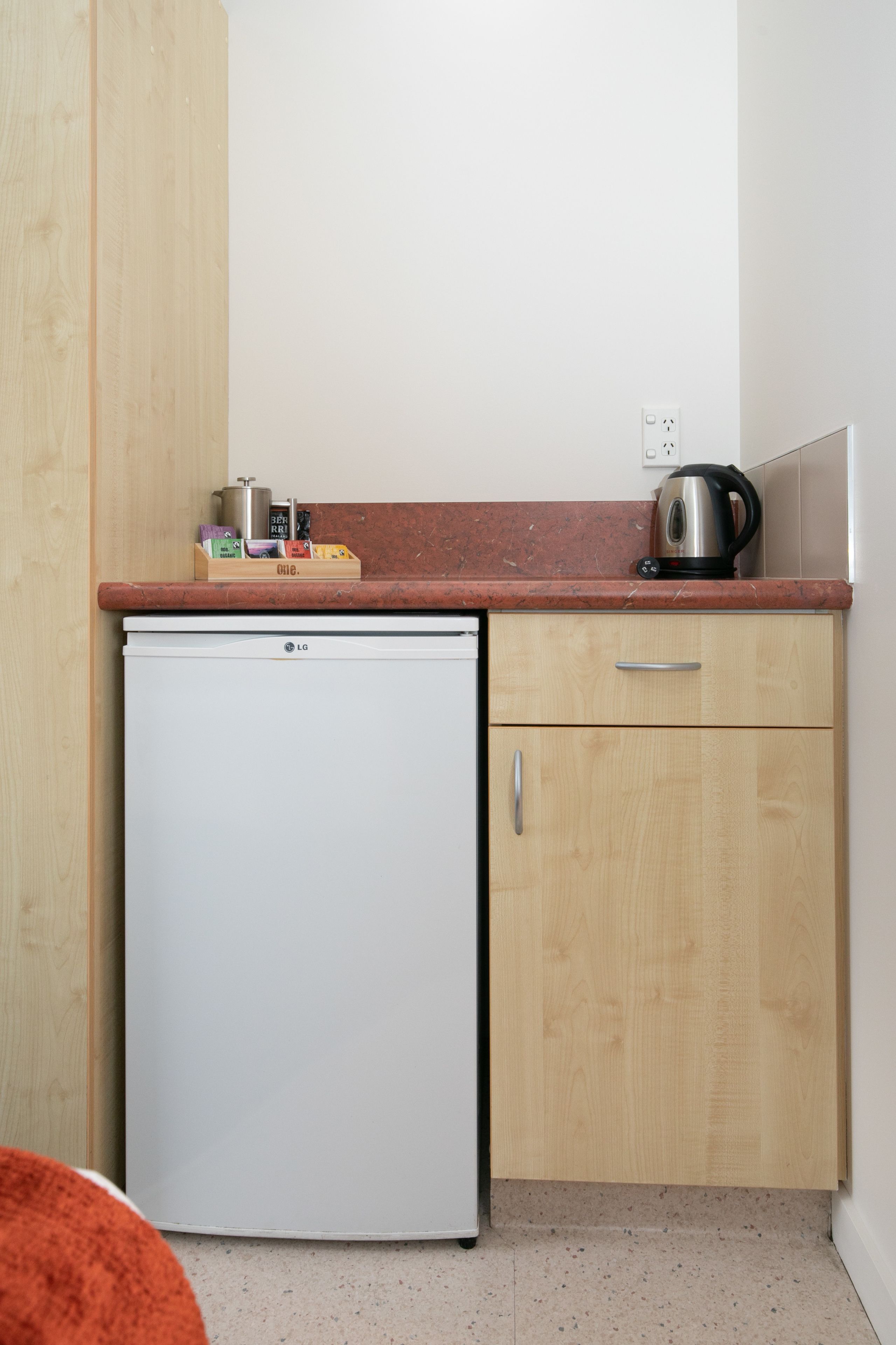 A compact kitchen with a white refrigerator, wooden cabinets, a marble countertop, and a kettle.