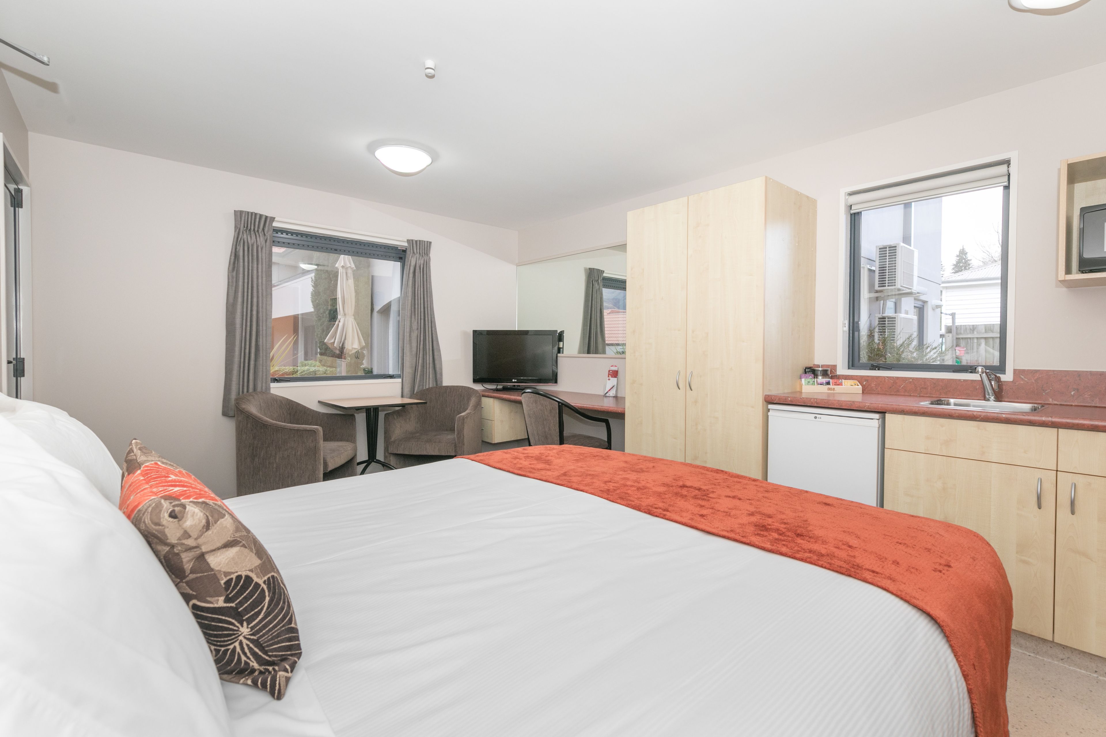 Hotelkamer met een bed, een bureau, een stoel, een televisie, een kleine koelkast en een raam met gordijnen.