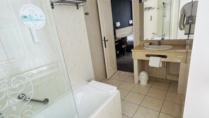 A modern bathroom with a bathtub, a sink, and a shower area. - Grand Hotel (Mayenne)