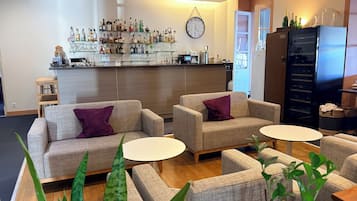 A bar area with a clock, sofas, and tables, and a refrigerator with bottles.
