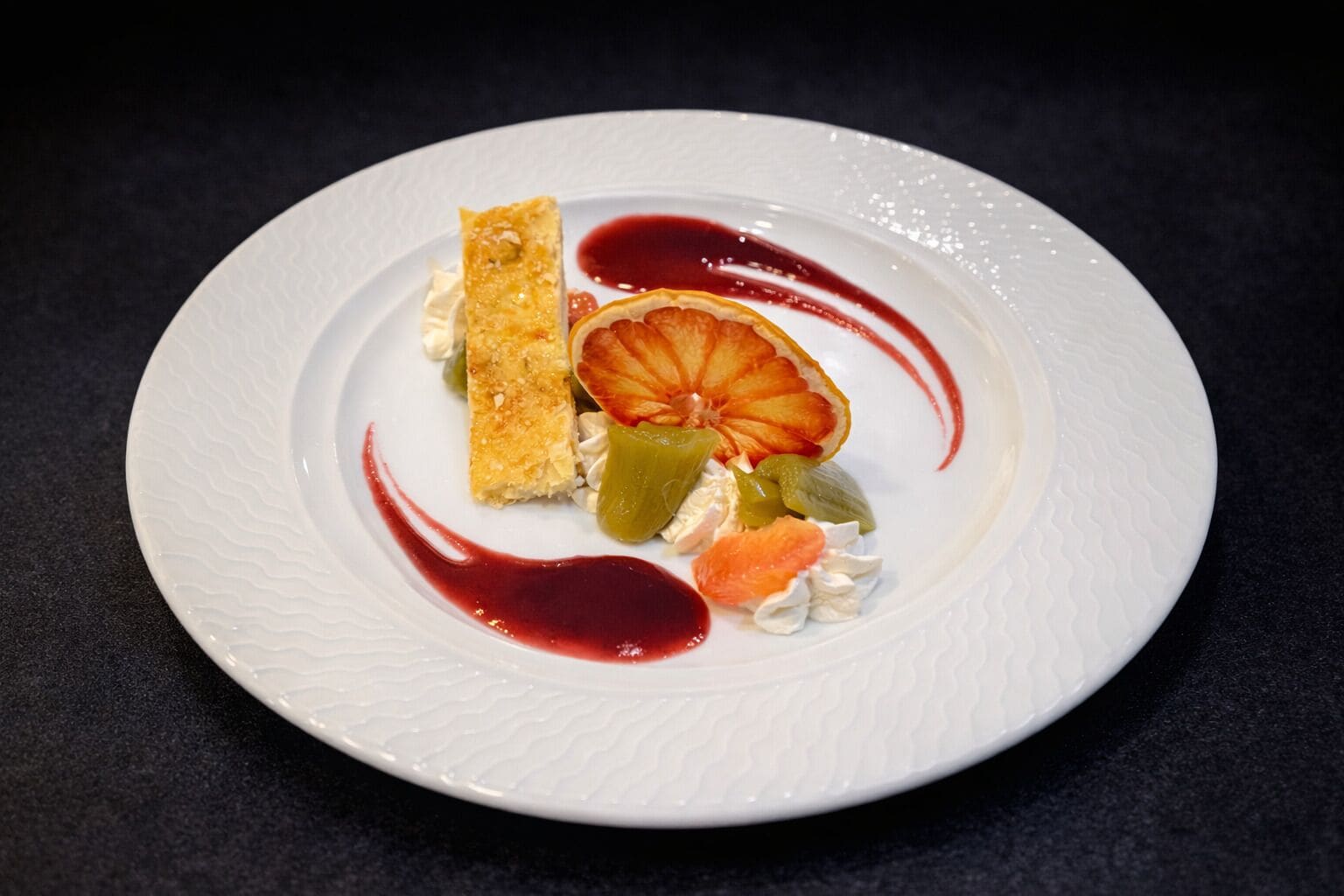 Ein weißer Teller mit einem Dessert aus Gebäck, Zitronenscheiben und einer roten Soße.