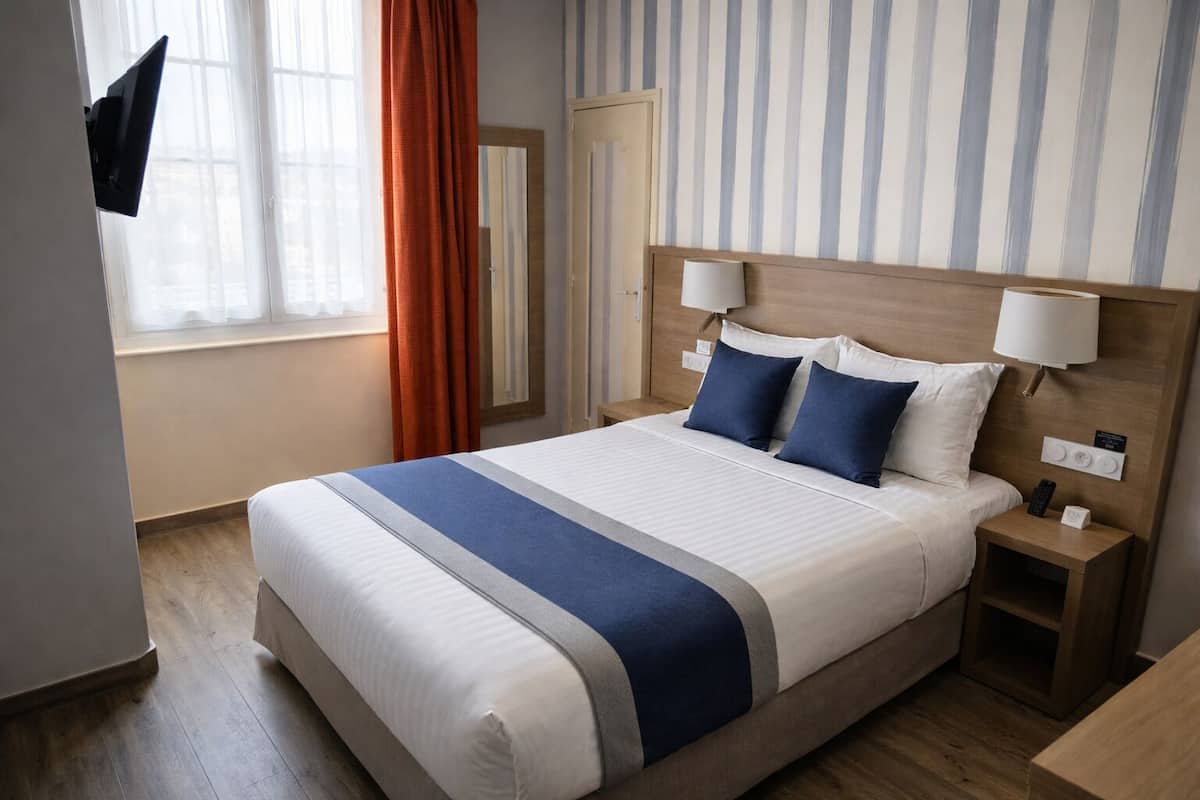 A hotel room with a large bed, two bedside tables, a TV mounted on the wall, and a window with curtains.