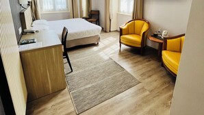 A hotel room with a bed, desk, two yellow armchairs, a TV, and a window with curtains. - Grand Hotel (Mayenne)