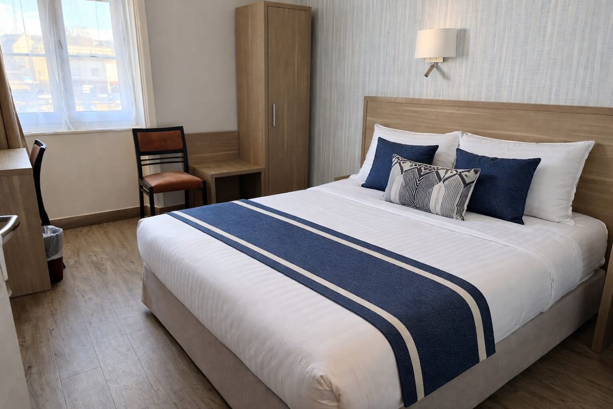 A hotel room with a large bed, a desk, a chair, a wardrobe, and a window with a view.