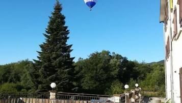 Un ballon à air chaud dans le ciel, au-dessus d’une terrasse en bois ornée de plantes en pot, avec une clôture en bois et un bâtiment en arrière-plan.