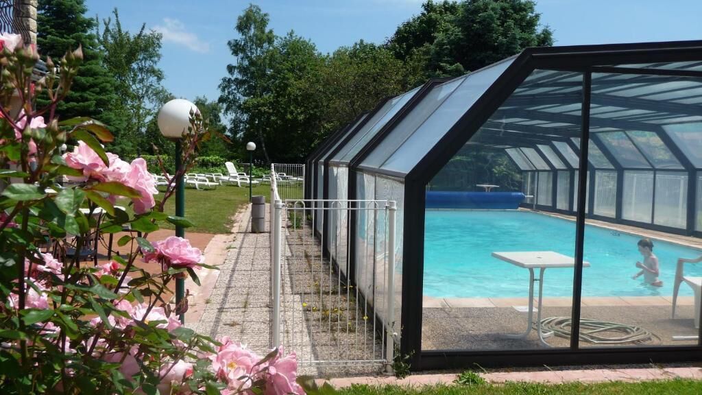 A swimming pool with a glass enclosure, surrounded by a garden with pink flowers.