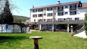 A multi-story building with a swimming pool, outdoor seating, and a covered patio area. - Logis La Rose des Vents (Volvic)