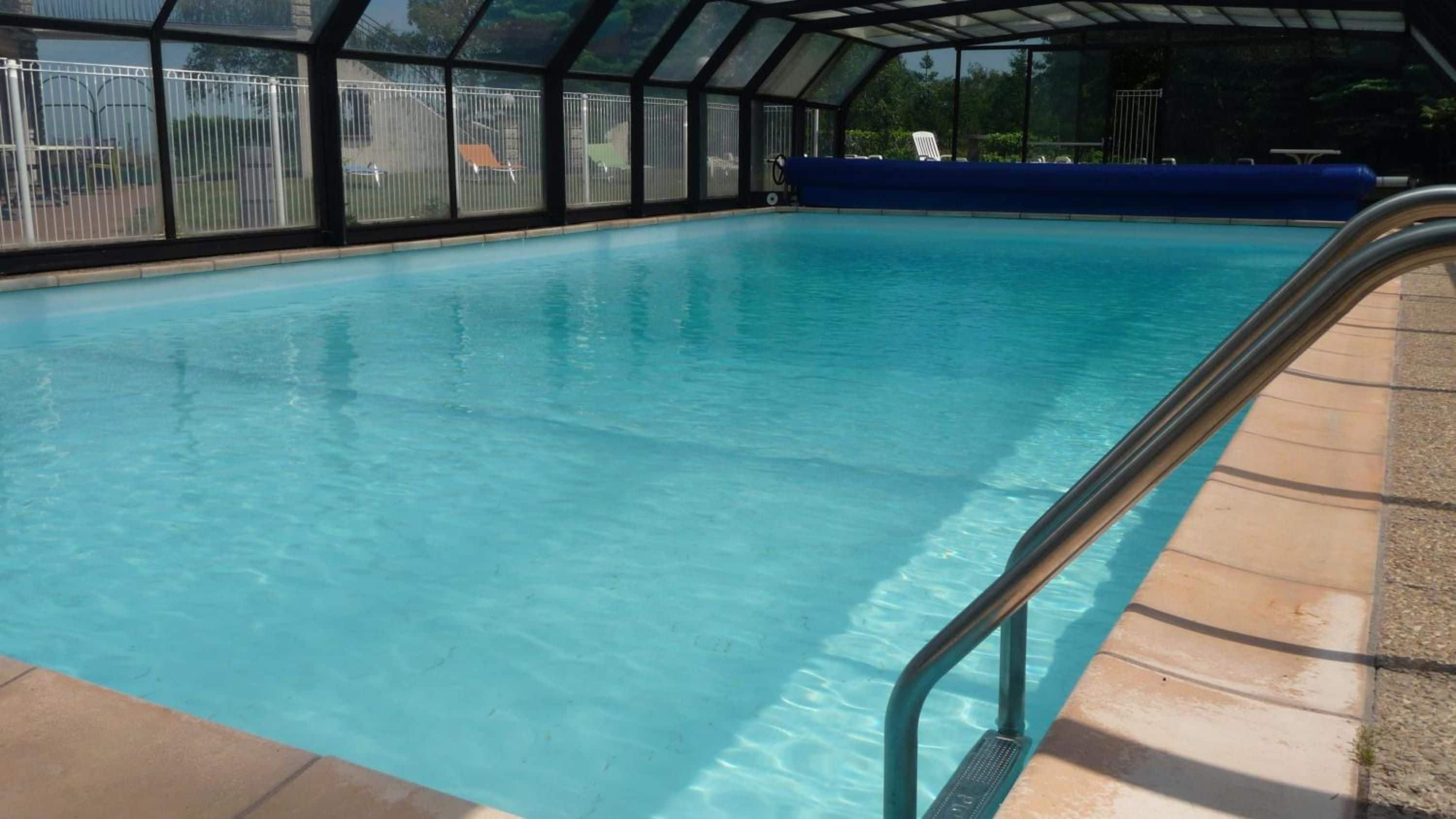 Una piscina interior transparente con una escalera metálica a la derecha.
