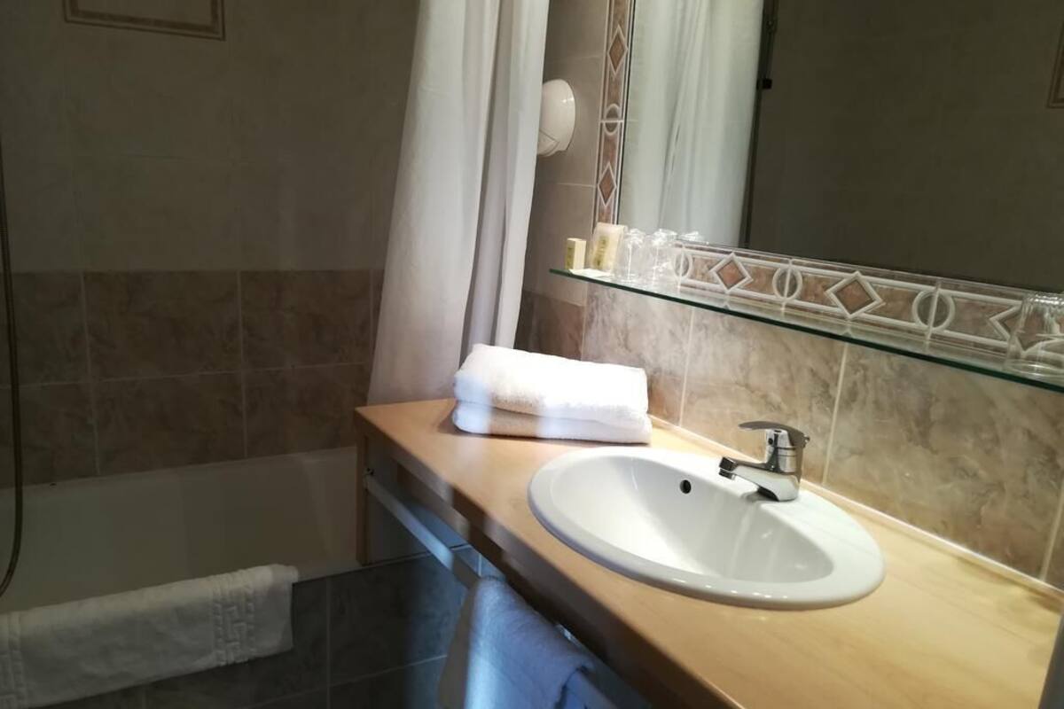 A bathroom with a beige tiled wall, a white sink, a glass shelf with toiletries, and a towel hanging on the wall.