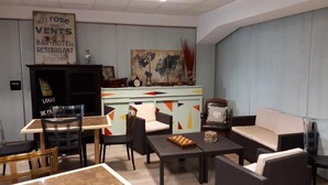 A living room with a sofa, chairs, a coffee table, and a dining area with a table and chairs. There is a world map artwork on the wall and a sign above the door. - Logis La Rose des Vents (Volvic)