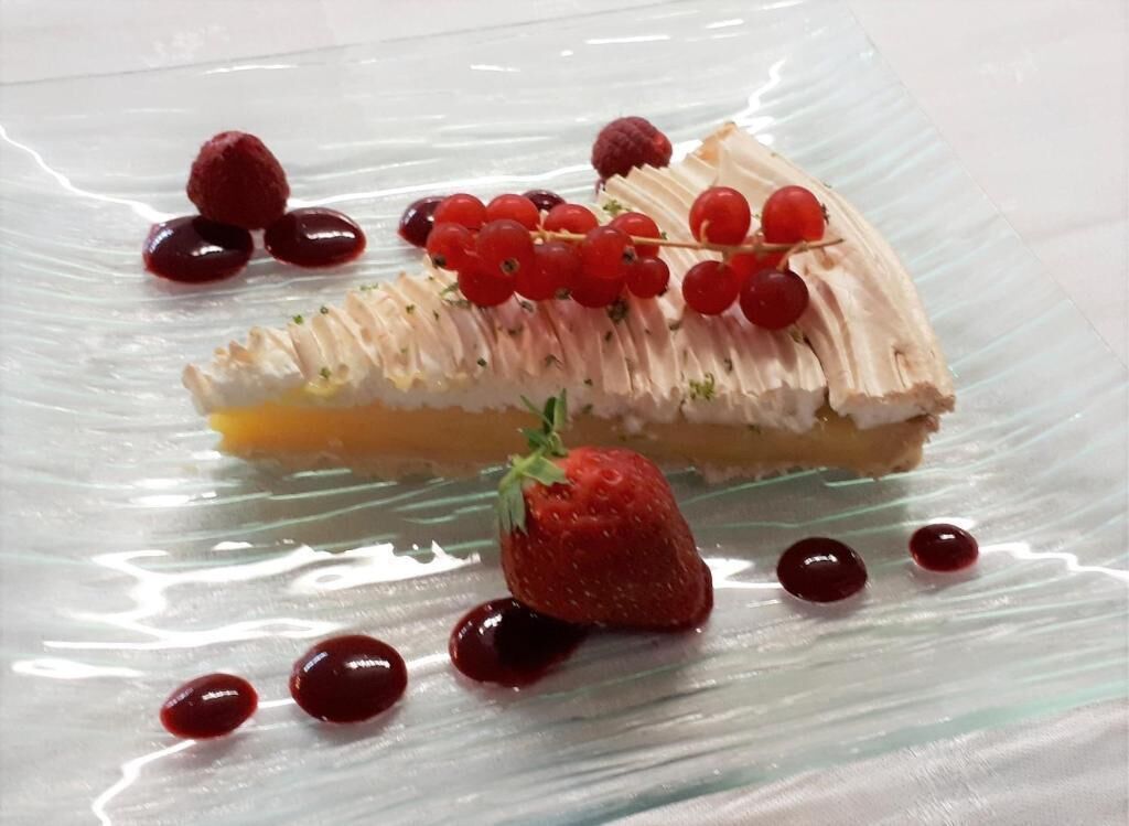 A slice of cake with berries on a clear glass plate.