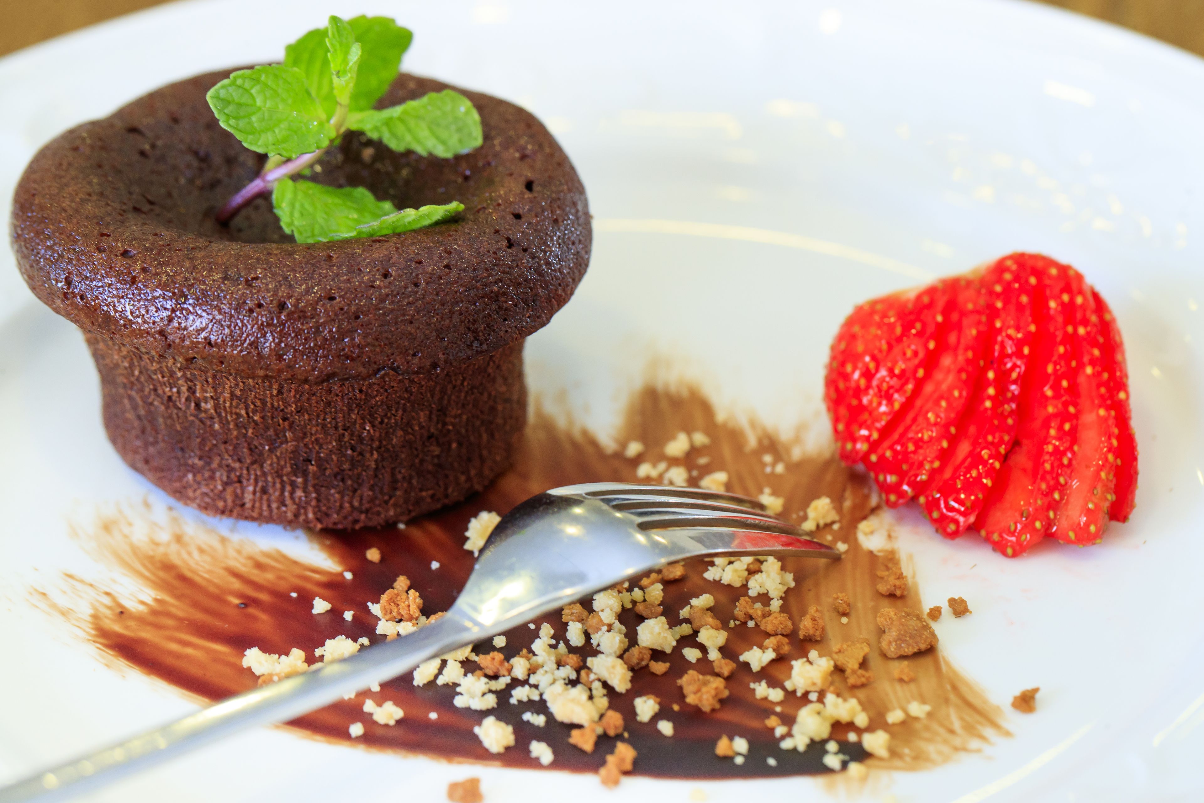 Un plato de postre con un pastel volcán de chocolate, una rebanada de fresa y cobertura desmenuzada.