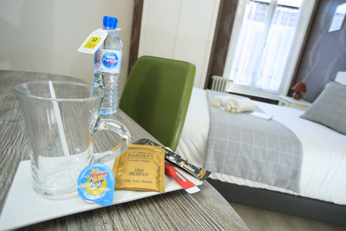 Ein Hotelzimmer mit einem Bett, einem Nachttisch mit einem Glas Wasser, einer Wasserflasche, einer Packung Frühstücksnahrung und einem grünen Sessel.