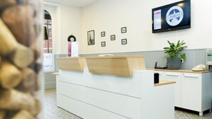 A reception area with a modern design, featuring a reception desk, a flat-screen TV, framed pictures on the wall, and a potted plant. - Hotel & Restaurant de la Basilique (Albert)