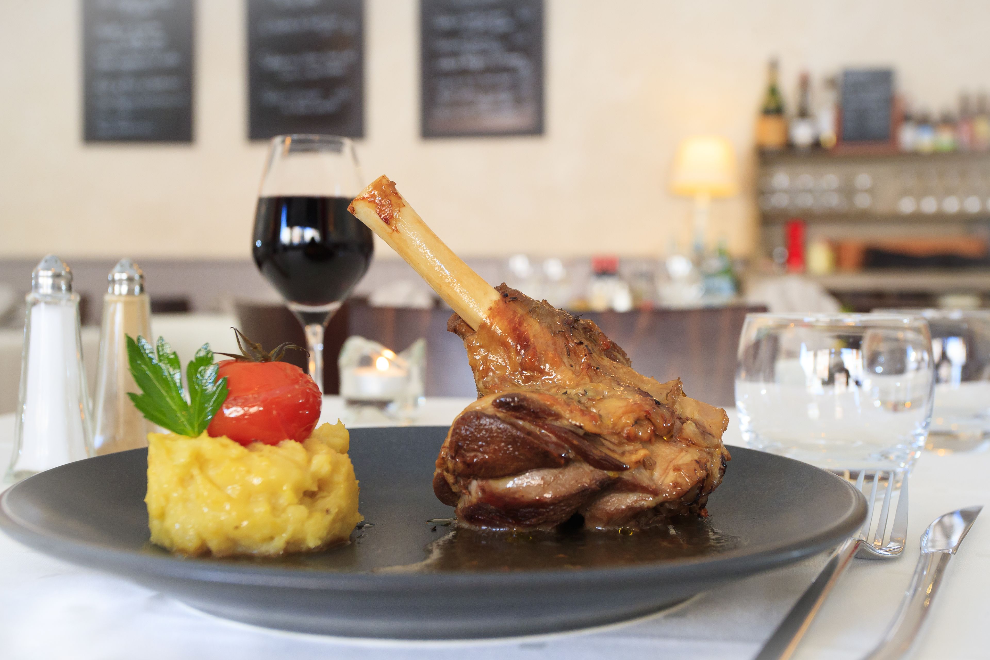 Une assiette comprenant un jarret d’agneau, de la purée de pommes de terre et une garniture de tomates cerises.