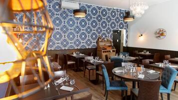 Un interior de restaurante con mesas y sillas de madera, papel tapiz estampado e iluminación colgante.